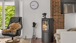 Ein modernes Wohnzimmer mit Kamin, einer Wanduhr und Blick ins Grüne.