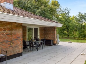 Un patio con un muro in mattoni, una zona relax coperta e un barbecue.