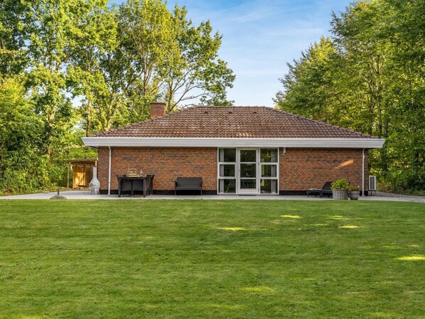 A brick house with a tiled roof, a covered patio, and a lawn.