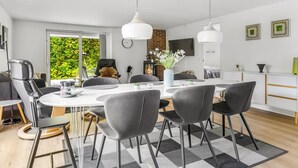 Ein moderner Essbereich mit einem weißen Tisch, grauen Stühlen und Pendelleuchten.