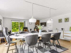 Zona pranzo moderna con tavolo bianco, sedie grigie e illuminazione a sospensione.
