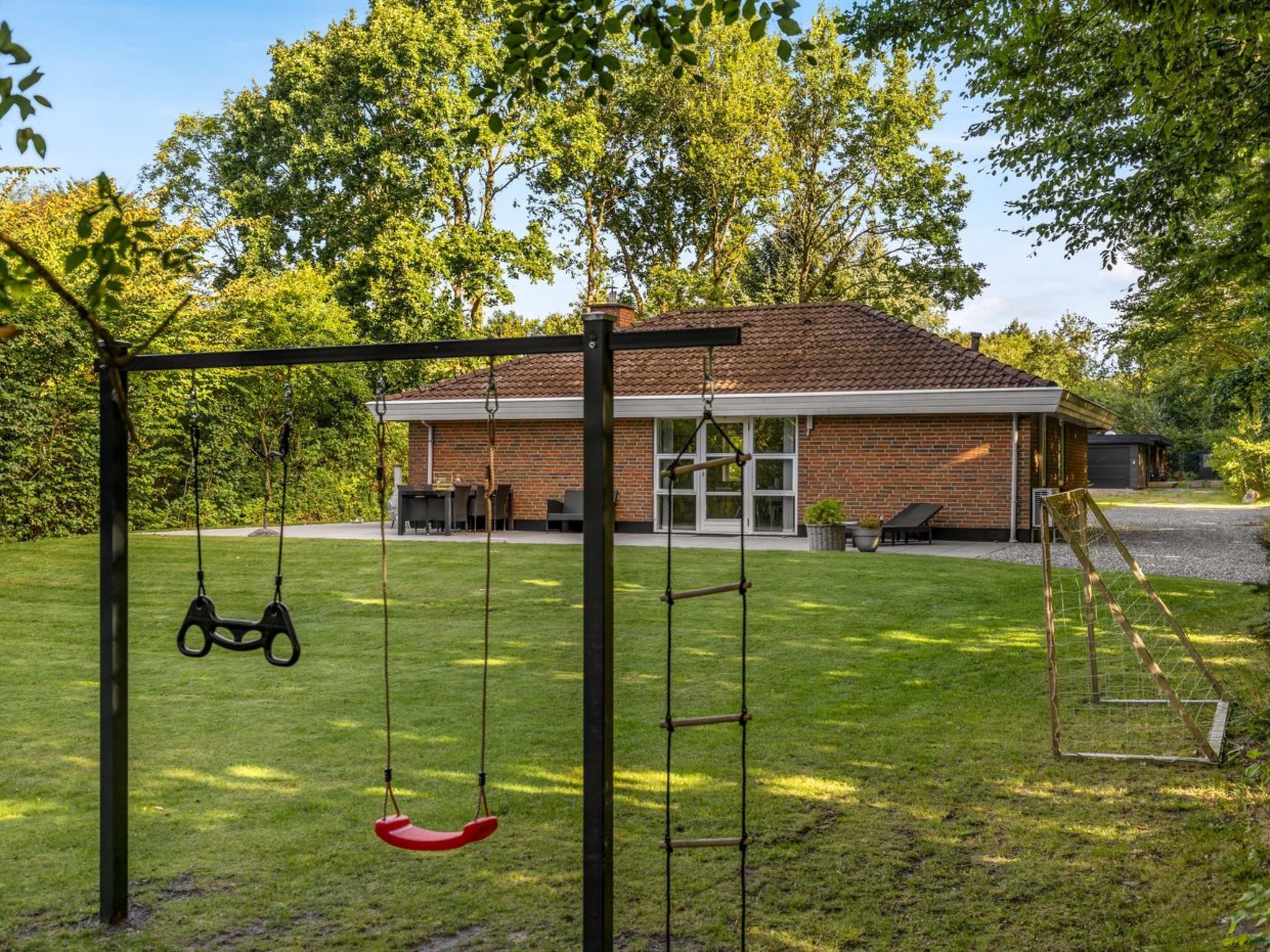 A backyard with a swing set, a brick house, and a lawn.