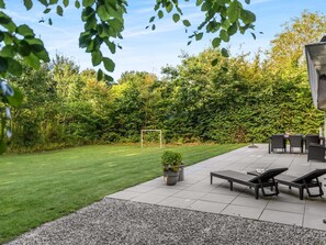 A patio area with a lawn, outdoor furniture, and a hedge.