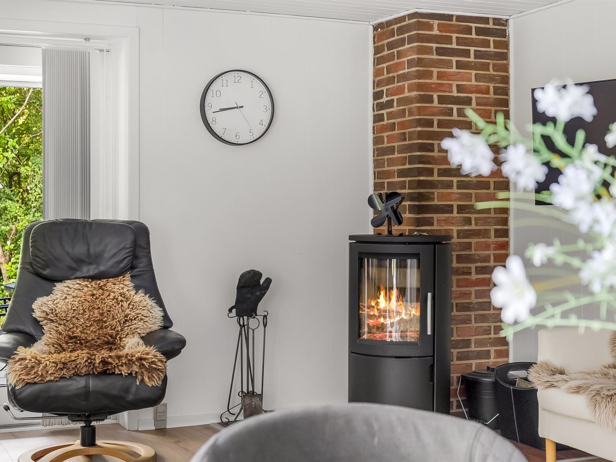 A living room with a black leather chair, a white sofa, a fireplace, a clock, and a window with blinds.