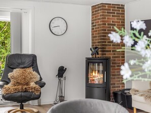 A living room with a black leather chair, a white sofa, a fireplace, a clock, and a window with blinds.