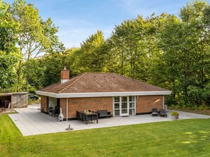 A single-story brick house with a covered patio area, a chimney, and a lawn.