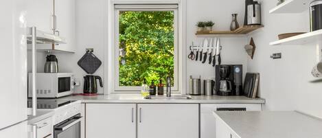 A modern kitchen with white cabinetry, a window with a view of greenery, and various appliances.