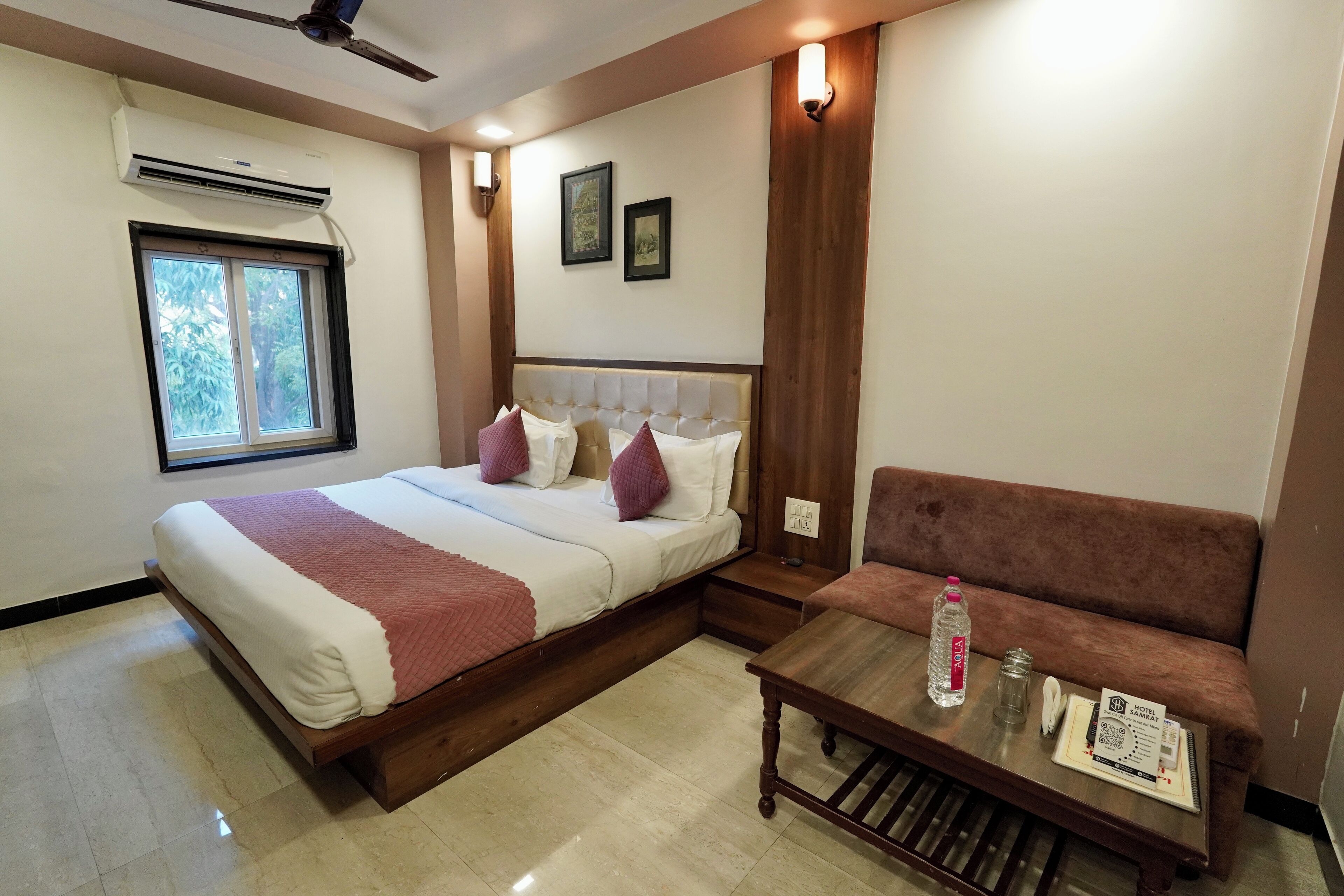 A hotel room with a bed, a sofa, a table with a water bottle, a phone, and a tray with a menu.
