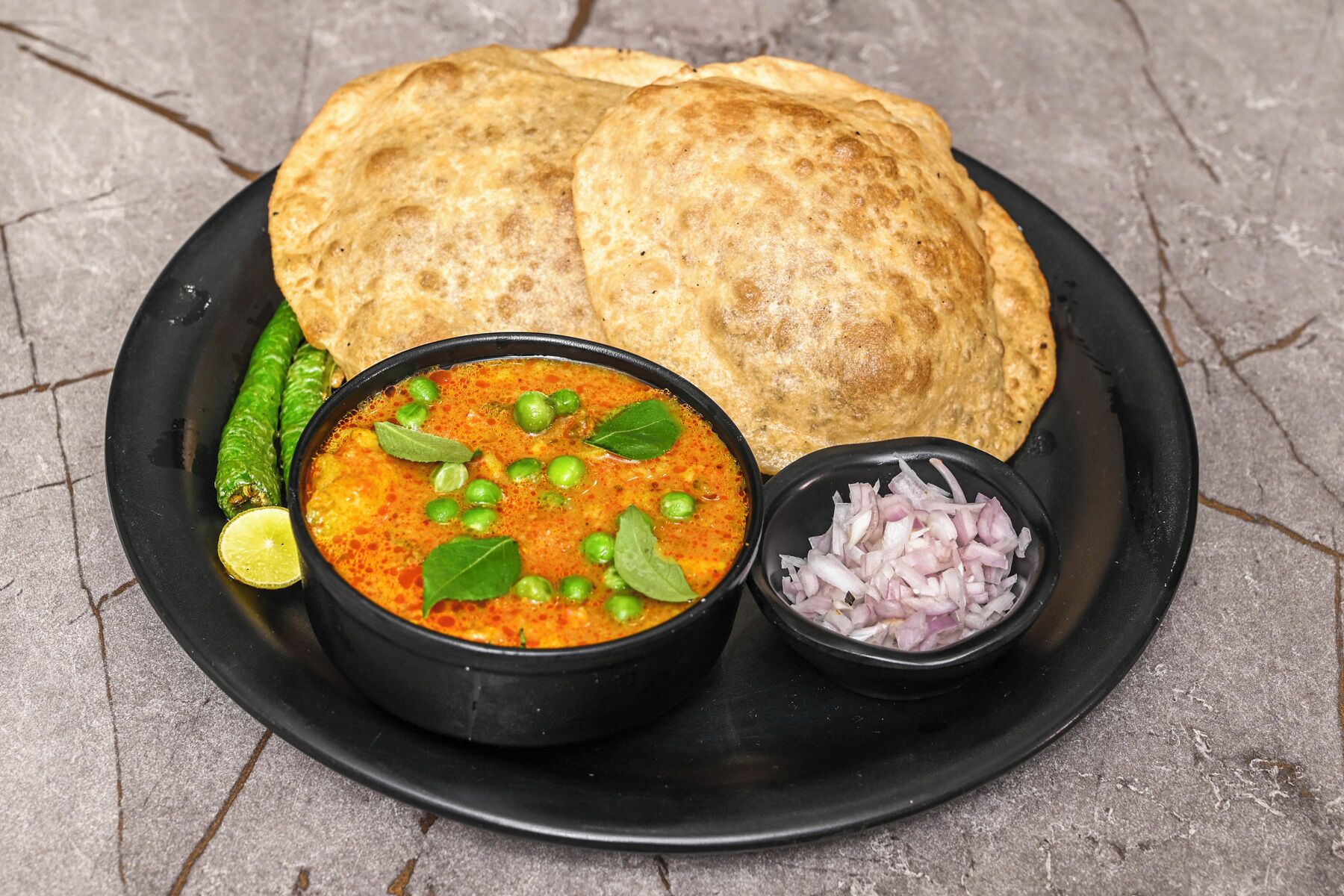 A plate with two pieces of flatbread, a bowl of curry with peas and lime, and a small bowl of sliced onions.
