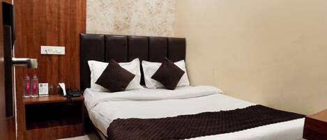 A neatly made bed with a dark headboard, a bedside table with a lamp, and a wall with floral wallpaper.