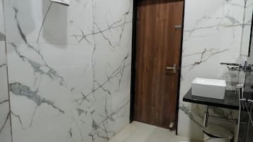 A bathroom with a marble wall, a wooden door, a white toilet, and a sink with a mirror.