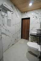 Un baño con pared de mármol, puerta de madera, inodoro blanco y lavabo con espejo.