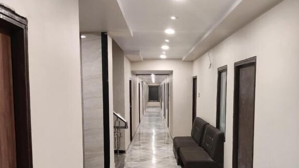 A long, narrow hallway with a marble floor, a sofa, and doors on both sides. - Hotel Samrat  (Ajmer)