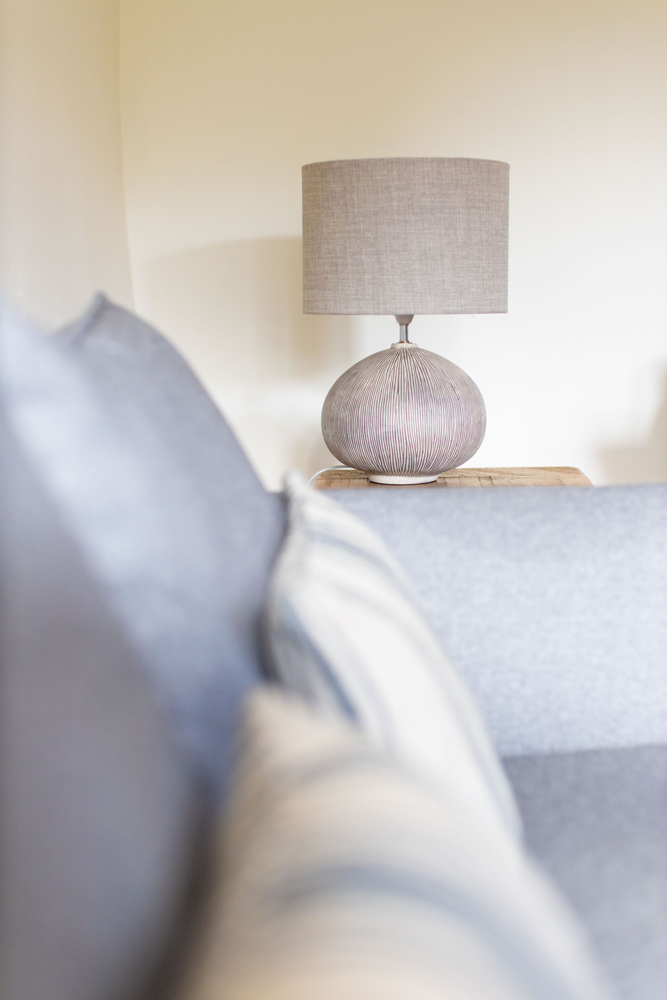 Un lit avec une couverture et des oreillers gris, une table de chevet avec une lampe et une tête de lit en bois.