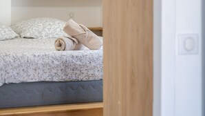 Un lit bien fait, recouvert d’une couvre-lit à motifs floraux, une serviette enroulée et un cadre photo posés sur la table de chevet.