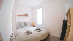 Un dormitorio con cama, mesita de noche, ventana y radiador.