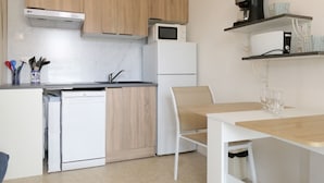 Una cocina compacta con muebles de madera, microondas, refrigerador, lavavajillas y una zona de comedor con mesa y sillas.