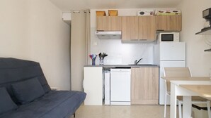 Cocina compacta con lavavajillas, microondas y un refrigerador pequeño. Hay una mesa de comedor con sillas y un sofá en la sala de estar.