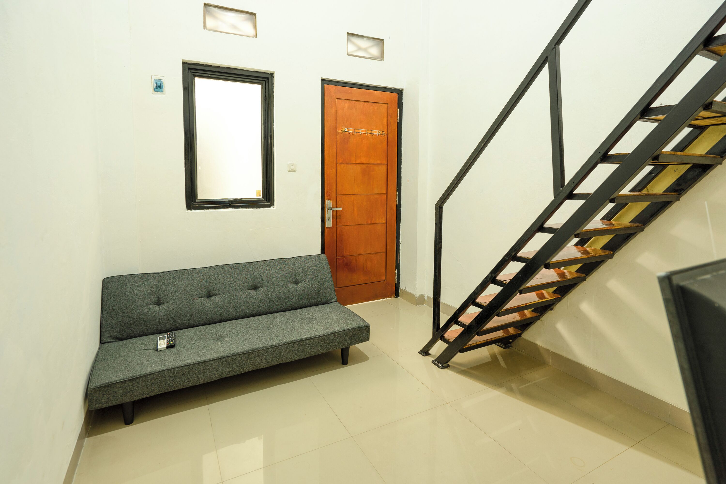 A hallway with a grey sofa, a wooden door, and a staircase with a metal railing.