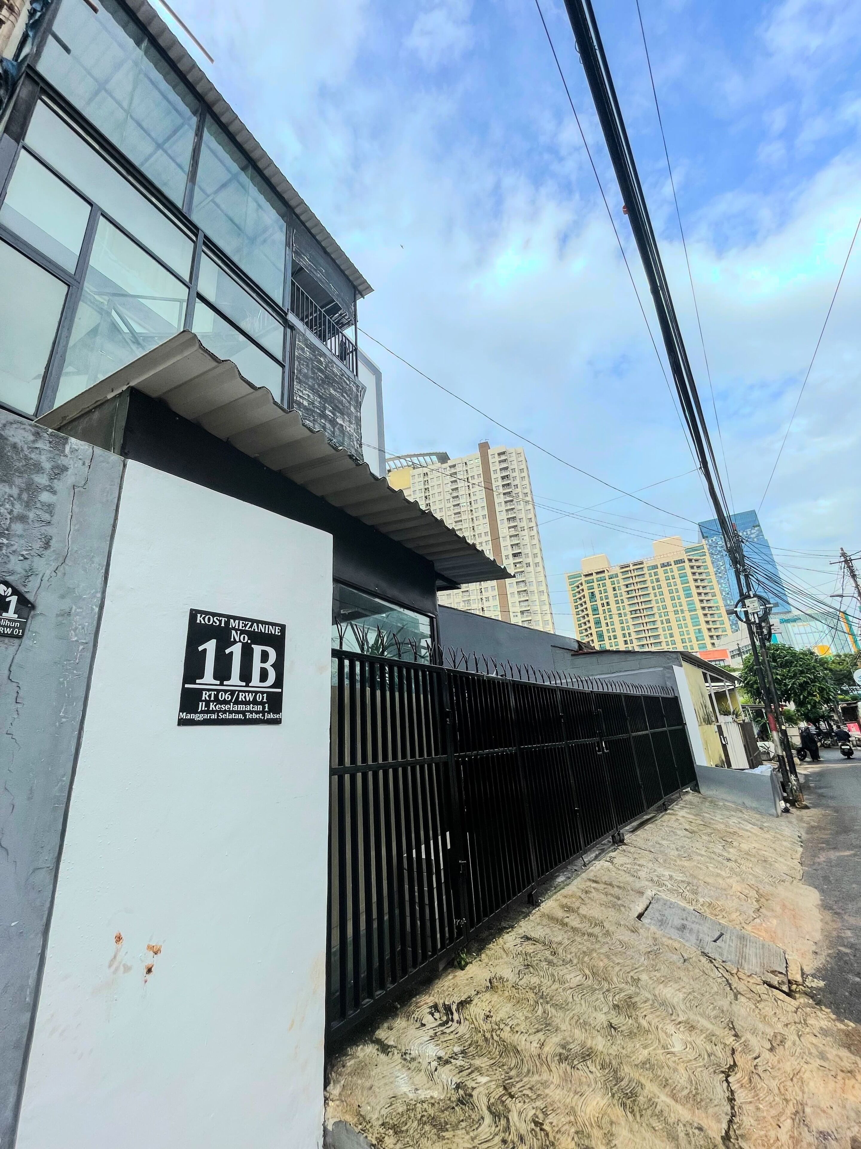 A building with a sign indicating 'KOST MEZANINE No. 11B RT 06 / RW 01 Jl. Keselamatan 1'.