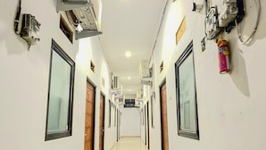 A hallway with air conditioning units, a fire extinguisher, and a security camera. - CQA Living By ARBA (Jakarta)