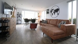 A spacious living room with a brown leather sofa, a wooden coffee table, and a dining area with a table and chairs. - Atmospheric Chalet Near the Wadden Sea (Tzummarum)
