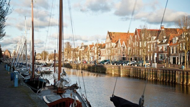 A canal with boats docked along the side, a row of traditional buildings, and a clear sky. - Atmospheric Chalet Near the Wadden Sea (Tzummarum)