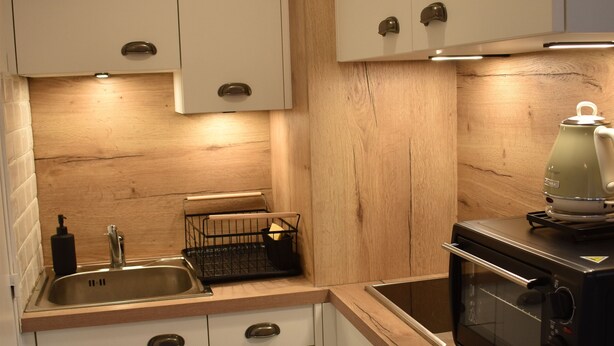 A kitchen with white cabinets, a wooden countertop, a sink, a kettle, and a microwave.