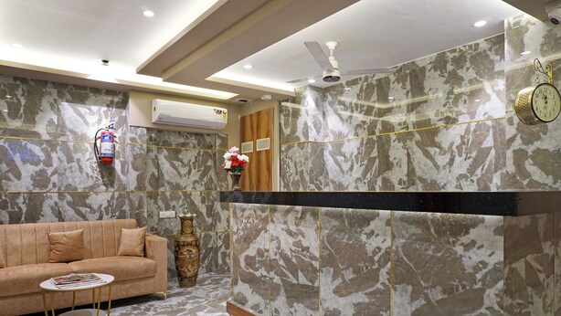 A modern lobby with a marble reception desk, a sofa, a small round table, and a decorative vase. - Hotel Nest Inn (Mumbai)