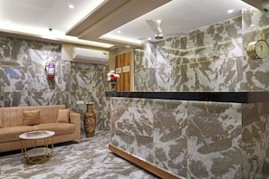 A modern lobby with a marble reception desk, a sofa, a small round table, and a decorative vase.