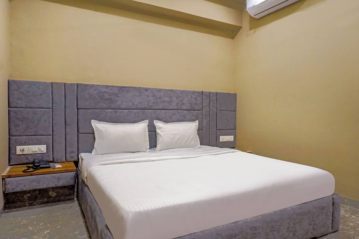A neatly made bed with a grey headboard, a bedside table with a lamp, and a wall-mounted air conditioner.
