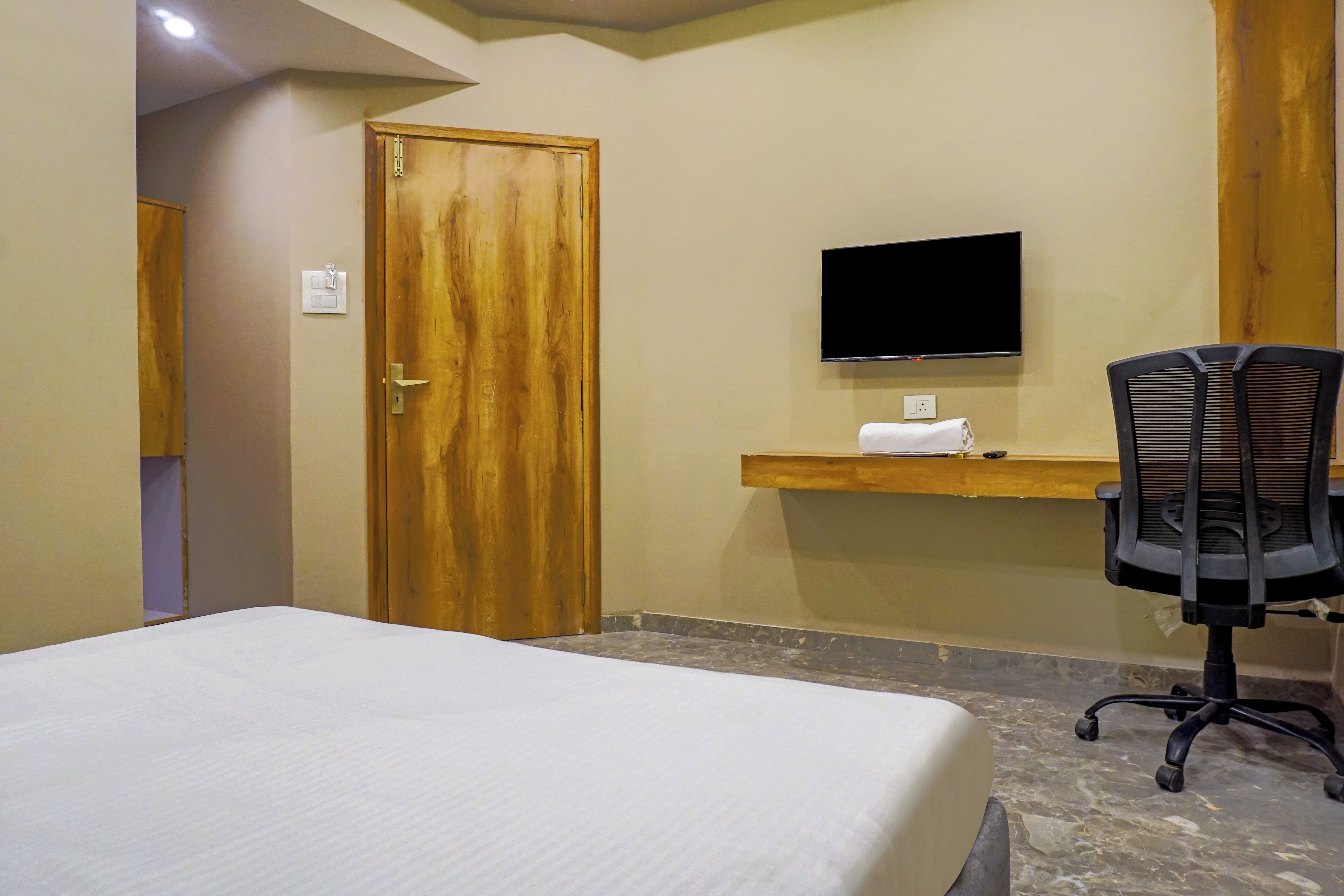 Ein Hotelzimmer mit einem Bett, einer Holztür, einem an der Wand befestigten Fernseher und einem Schreibtisch mit Stuhl.