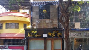A hotel named 'Hotel Nest Inn' with a signboard in English and Hindi, a parked scooter, and a tree in front. - Hotel Nest Inn (Mumbai)