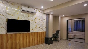 A modern reception area with a marble wall, a mounted TV, a wooden reception desk, a black office chair, and a sofa in the background. - Hotel Nest Inn (Mumbai)
