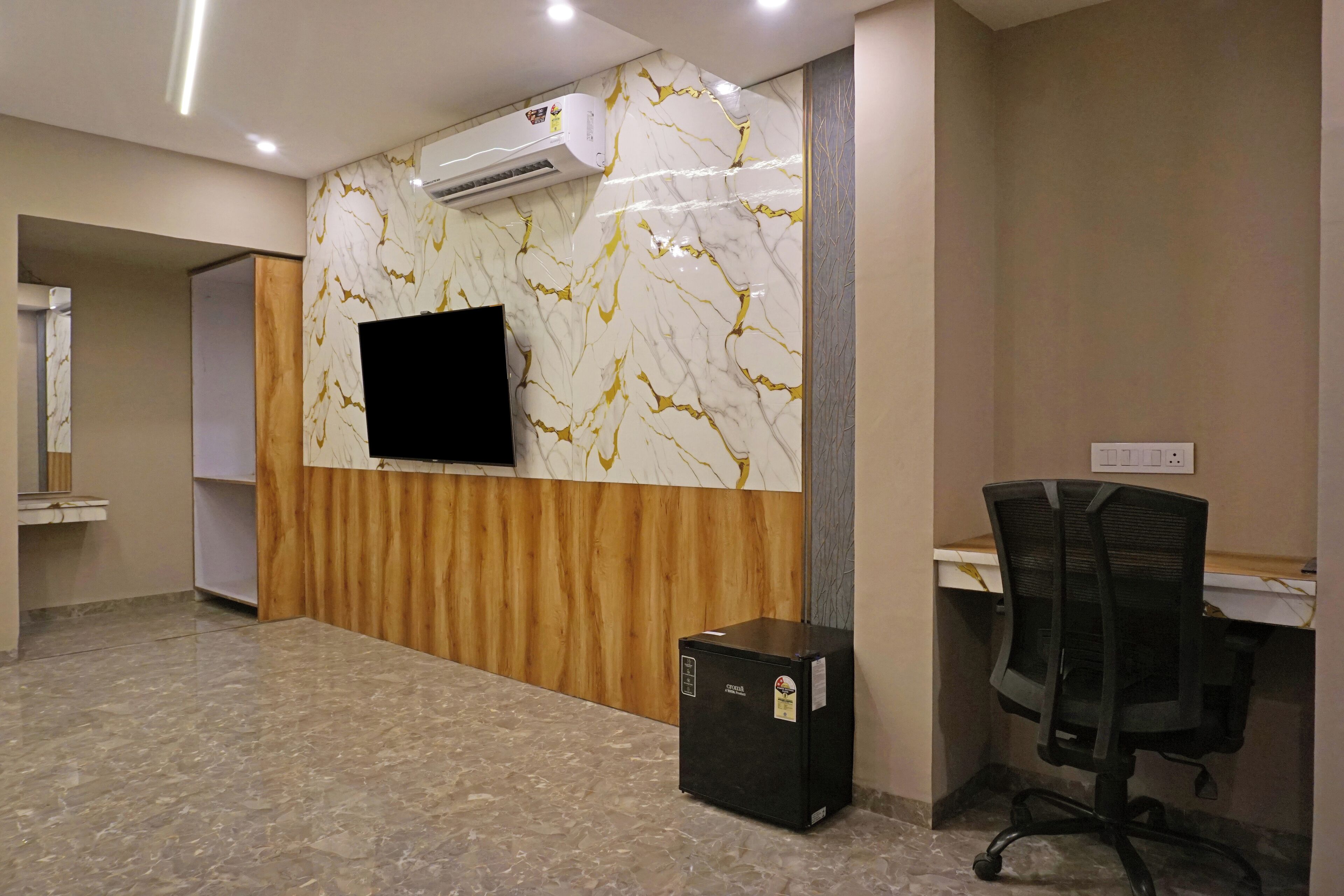 A reception area with a marble wall, a mounted TV, a wooden panel, a black office chair, and a small black cabinet.