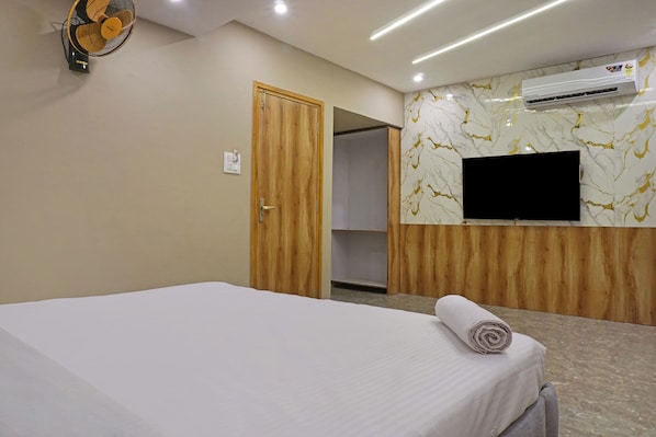 A hotel room with a bed, a wall-mounted air conditioner, a television, and a wooden wardrobe.