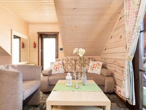 A cozy room with a wooden ceiling, a sofa with floral cushions, a small table with a vase and a lantern, and a window with curtains. - Comfortable Apartment Close to the Beach (Ustronie Morskie)