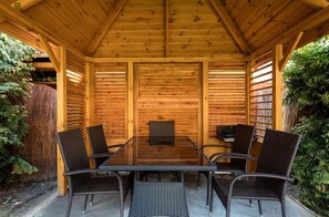 Eine überdachte Holzterrasse mit Tisch und Stühlen, umgeben von Bücherregalen.