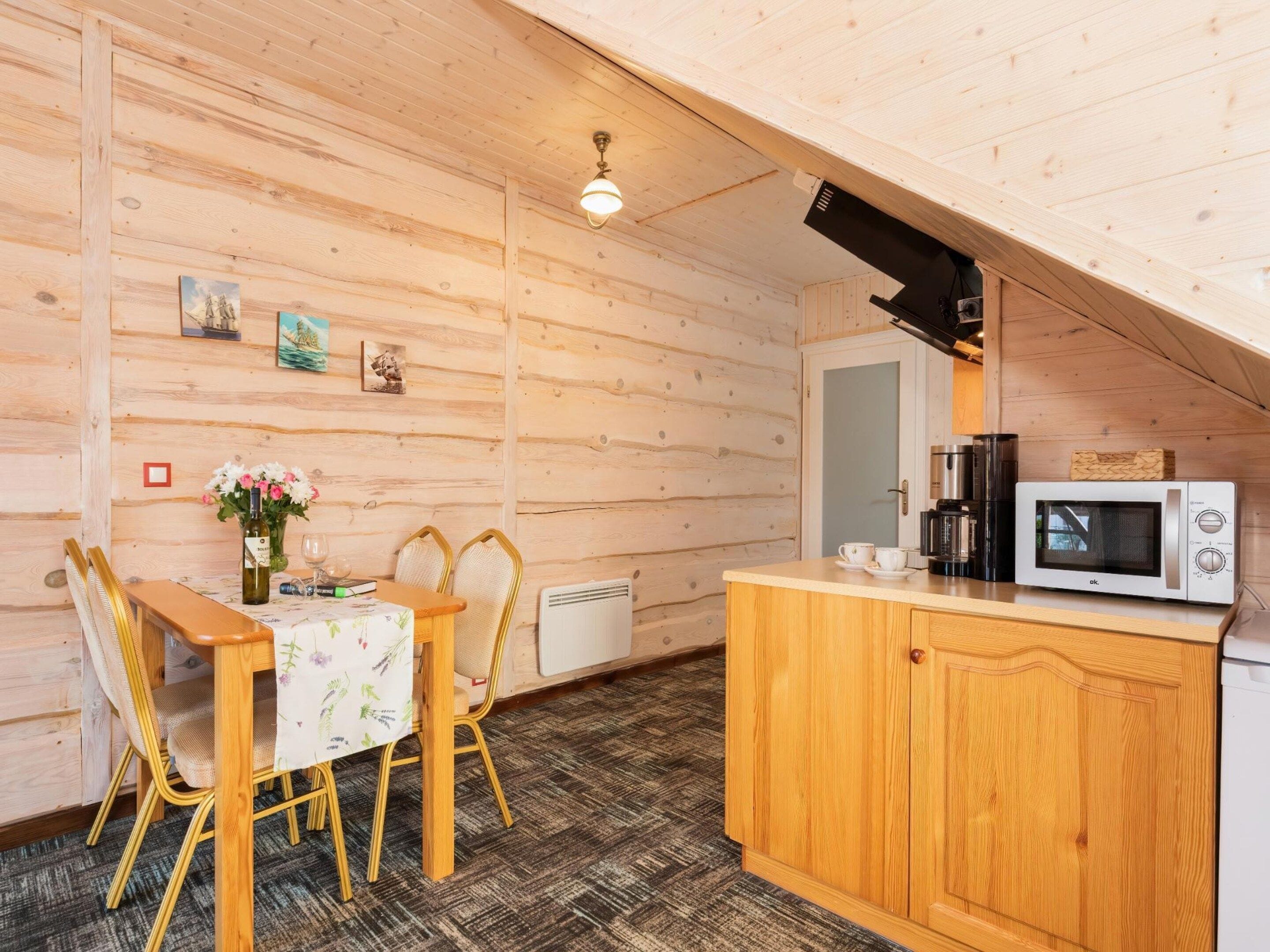 A cozy cabin interior with a wooden dining table, chairs, a small kitchen area with a microwave, and a coffee maker.