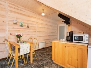 A cozy cabin interior with a wooden dining table, chairs, a small kitchen area with a microwave, and a coffee maker. - Comfortable Apartment Close to the Beach (Ustronie Morskie)