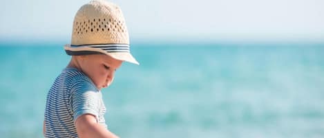A child playing with toys on a sandy beach with the ocean in the background.