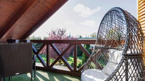 Eine Holzterrasse mit einer Hängematte und einem Korbstuhl, mit Blick auf einen Garten mit Baum und Zaun.