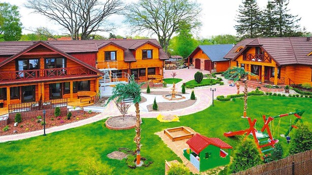Eine Holzhütte mit mehreren Blockhütten, einem zentralen Innenhof mit einem Brunnen und einem eingezäunten Spielplatz.