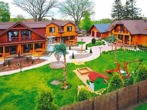 A lodge with multiple wooden cabins, a central courtyard with a fountain, and a fenced play area. - Comfortable Apartment Close to the Beach (Ustronie Morskie)