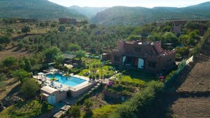 Eine Villa mit Swimmingpool, umgeben von üppiger Vegetation und Bergen im Hintergrund.