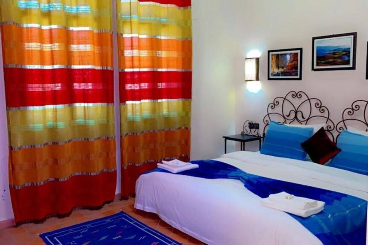 Ein Hotelzimmer mit Bett, Vorhängen, einem Sessel, einem kleinen Tisch und Wandleuchten.
