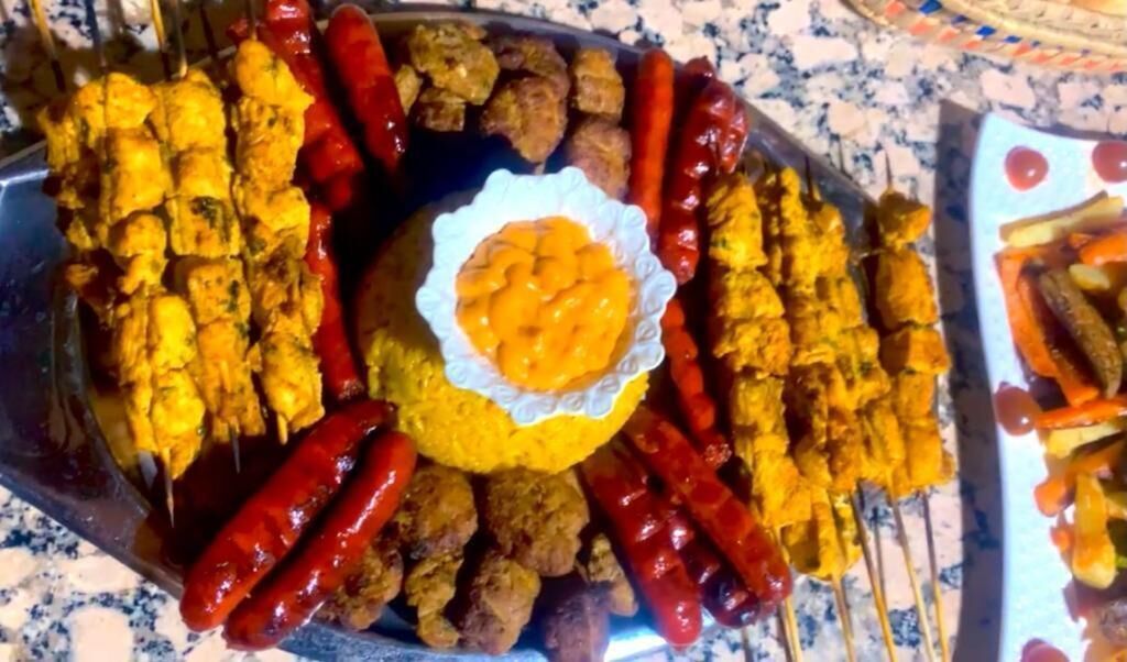 Une grande assiette contenant diverses brochettes de viande et de légumes, notamment des saucisses, des poivrons et, éventuellement, du poulet, disposées sur une table.