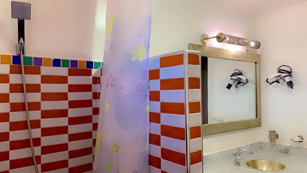 A bathroom with a checkered tile wall, a shower, a sink with a gold faucet, and a mirror with a decorative frame.