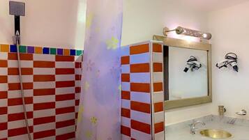 A bathroom with a checkered tile wall, a shower, a sink with a gold faucet, and a mirror with a decorative frame.