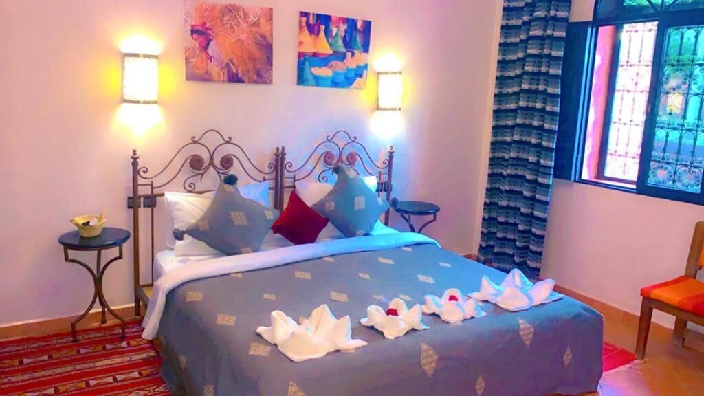 Un lit avec une couvre-lit bleue, des oreillers et des cygnes décoratifs. On y trouve également des lampes fixées au mur, une fenêtre avec vue et un fauteuil.